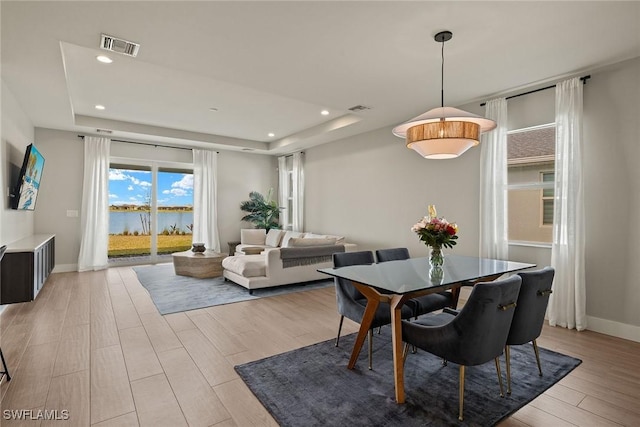 dining room featuring a water view, a tray ceiling, and light hardwood / wood-style floors