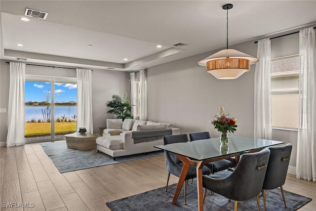 dining space featuring a water view, a raised ceiling, and light hardwood / wood-style floors