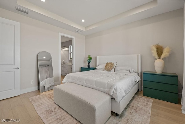 bedroom featuring hardwood / wood-style floors, a raised ceiling, and ensuite bathroom