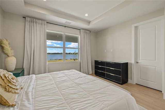 bedroom featuring a water view, a raised ceiling, and hardwood / wood-style floors