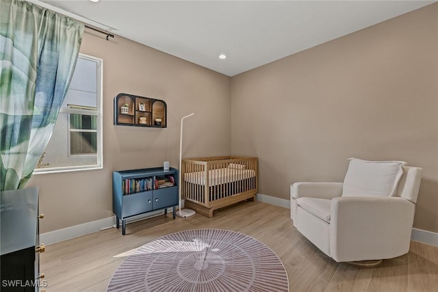 bedroom featuring a nursery area and light hardwood / wood-style flooring