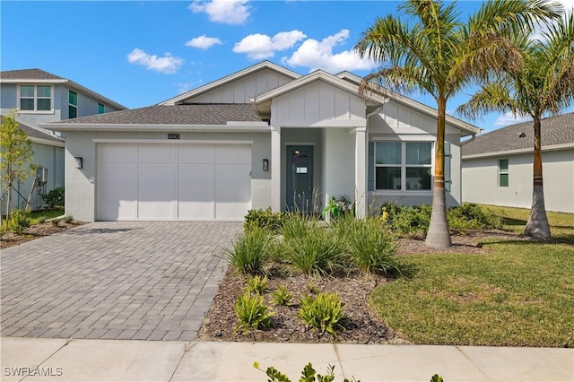 view of front of home featuring stucco siding, decorative driveway, board and batten siding, a front yard, and an attached garage