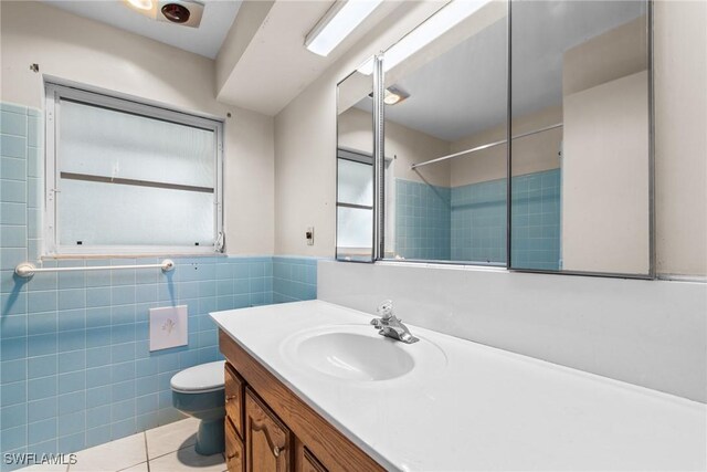 full bath with wainscoting, toilet, tile patterned flooring, vanity, and tile walls