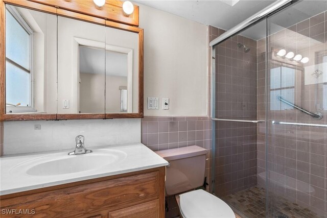 full bathroom featuring a wainscoted wall, tile walls, toilet, vanity, and a shower stall