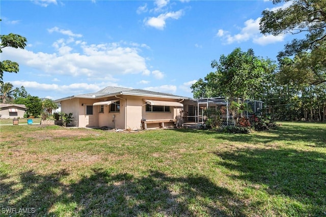 back of house with glass enclosure, a yard, and stucco siding