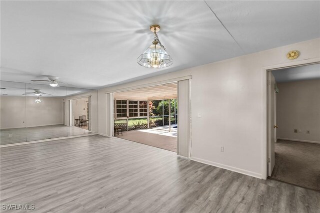 unfurnished living room featuring ceiling fan with notable chandelier, wood finished floors, and baseboards