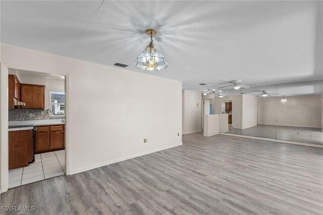 unfurnished living room with light wood-type flooring, visible vents, ceiling fan, and baseboards