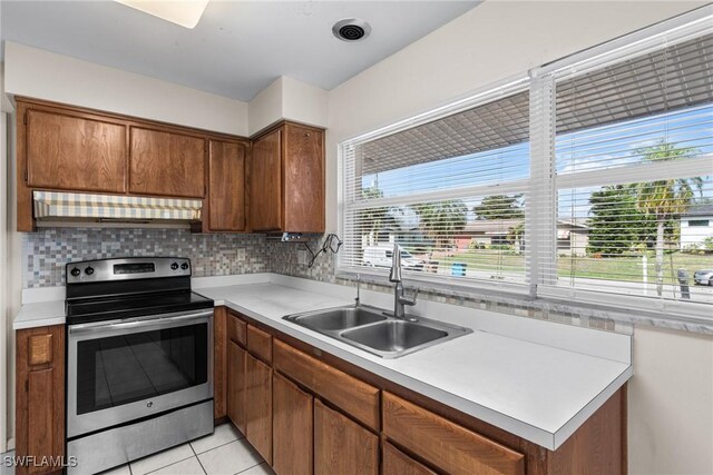 kitchen featuring under cabinet range hood, a sink, light countertops, decorative backsplash, and stainless steel electric range oven