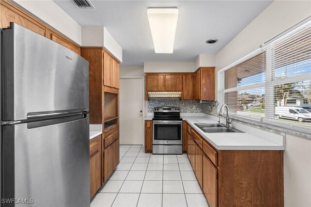 kitchen featuring brown cabinets, light tile patterned floors, stainless steel appliances, a sink, and under cabinet range hood