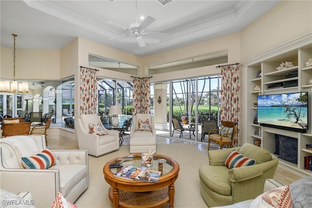 living room featuring ceiling fan with notable chandelier, a tray ceiling, a fireplace, and built in features