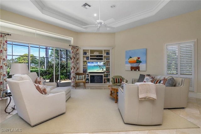 living area with light tile patterned floors, visible vents, ceiling fan, ornamental molding, and a tray ceiling