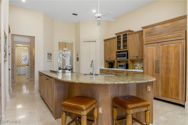 kitchen with a breakfast bar area, stainless steel microwave, glass insert cabinets, brown cabinetry, and light stone countertops