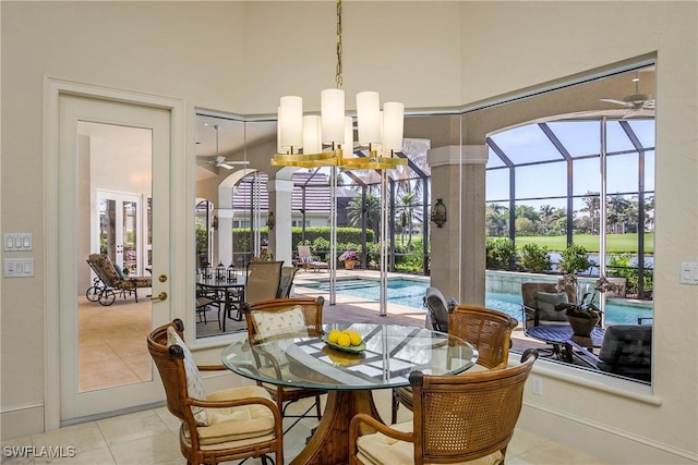 dining space with a sunroom, a high ceiling, light tile patterned flooring, and ceiling fan with notable chandelier