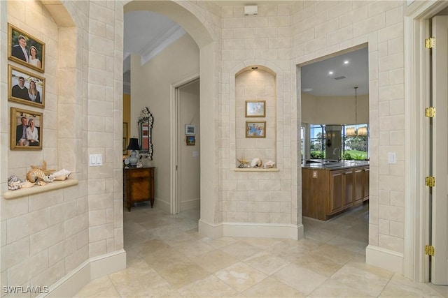 hallway with arched walkways, tile walls, baseboards, and light tile patterned floors