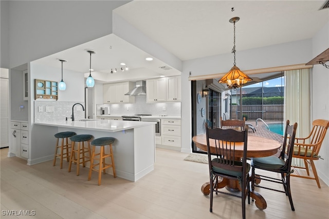 kitchen featuring sink, white cabinetry, decorative light fixtures, wall chimney exhaust hood, and kitchen peninsula