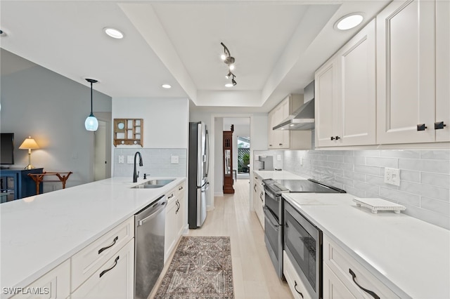 kitchen with sink, white cabinetry, wall chimney range hood, stainless steel appliances, and hanging light fixtures