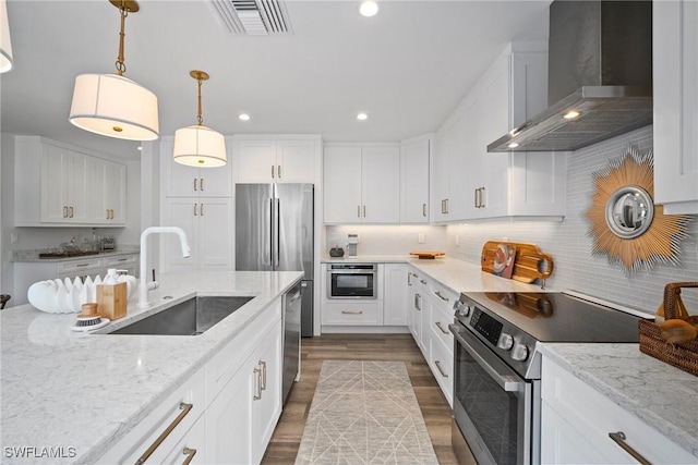 kitchen featuring visible vents, white cabinets, wall chimney exhaust hood, stainless steel appliances, and a sink