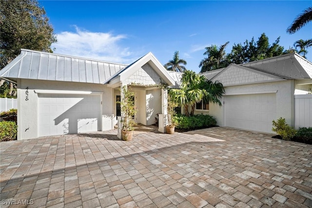 view of front of house featuring a garage, metal roof, a standing seam roof, decorative driveway, and stucco siding