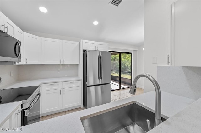 kitchen featuring sink, appliances with stainless steel finishes, white cabinetry, light stone countertops, and decorative backsplash