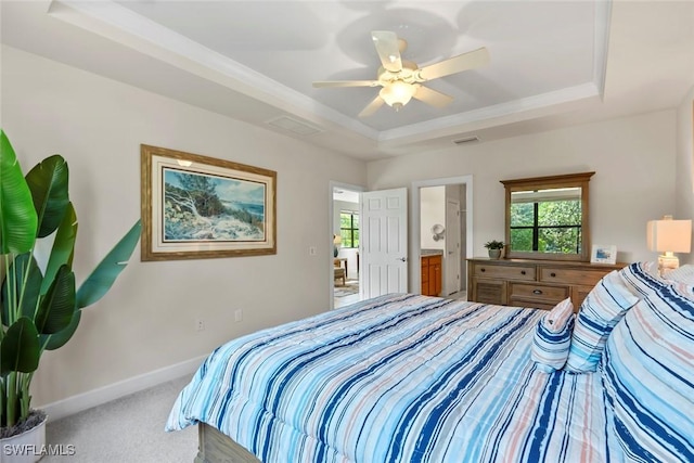 bedroom featuring ceiling fan, ensuite bath, a tray ceiling, and carpet