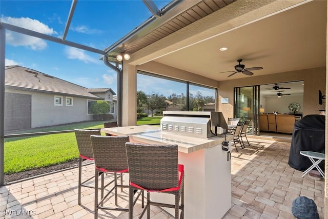 view of patio / terrace with area for grilling, an outdoor bar, grilling area, ceiling fan, and glass enclosure