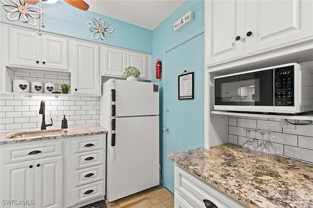 kitchen with a textured ceiling, white appliances, a sink, white cabinets, and light stone countertops