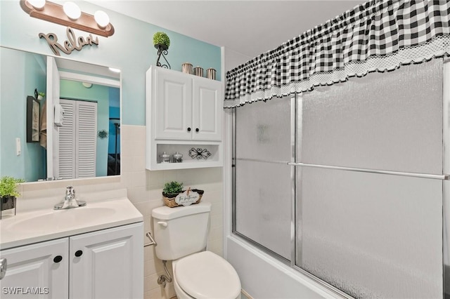 bathroom featuring enclosed tub / shower combo, toilet, vanity, and tile walls