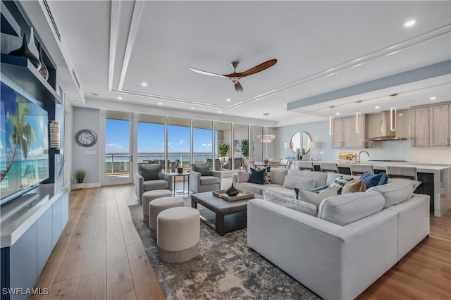 living room featuring a raised ceiling, ceiling fan, sink, and light hardwood / wood-style floors