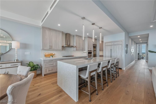 kitchen with wall chimney exhaust hood, gas stovetop, decorative light fixtures, a center island with sink, and light hardwood / wood-style floors