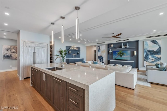 kitchen with sink, light hardwood / wood-style flooring, paneled built in refrigerator, an island with sink, and light stone countertops