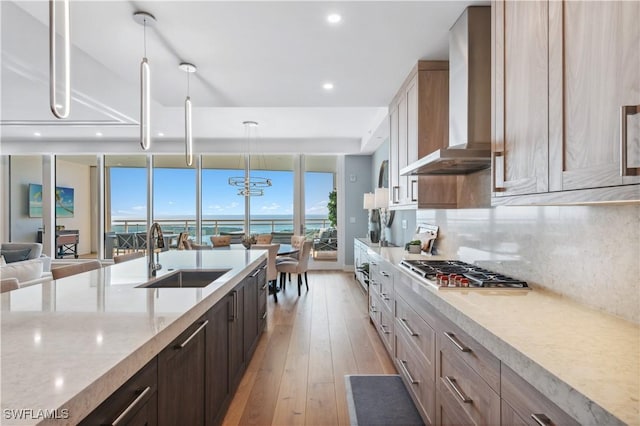 kitchen with sink, decorative light fixtures, stainless steel gas stovetop, light stone countertops, and wall chimney range hood