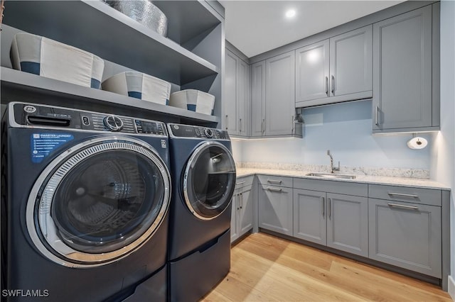 washroom with cabinets, washing machine and clothes dryer, sink, and light hardwood / wood-style flooring