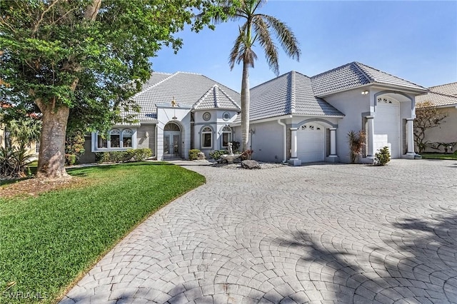 french provincial home featuring a garage, a tiled roof, decorative driveway, a front yard, and stucco siding