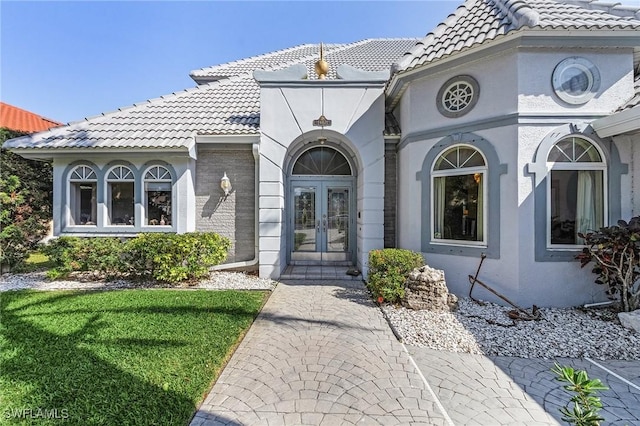 property entrance featuring french doors, a tile roof, brick siding, and stucco siding