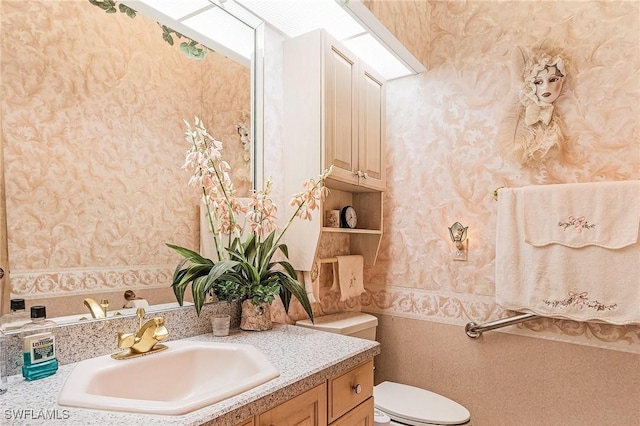 bathroom featuring vanity, toilet, and wallpapered walls