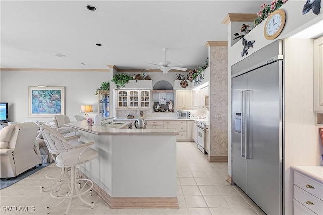 kitchen featuring built in appliances, crown molding, a kitchen bar, a sink, and light tile patterned flooring