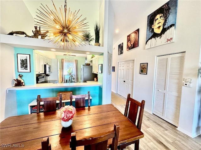 dining area with a towering ceiling, a chandelier, sink, and light wood-type flooring