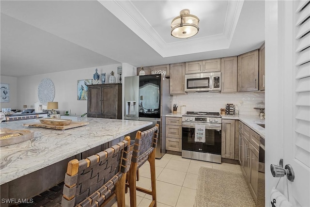 kitchen featuring appliances with stainless steel finishes, tasteful backsplash, ornamental molding, light tile patterned floors, and a raised ceiling