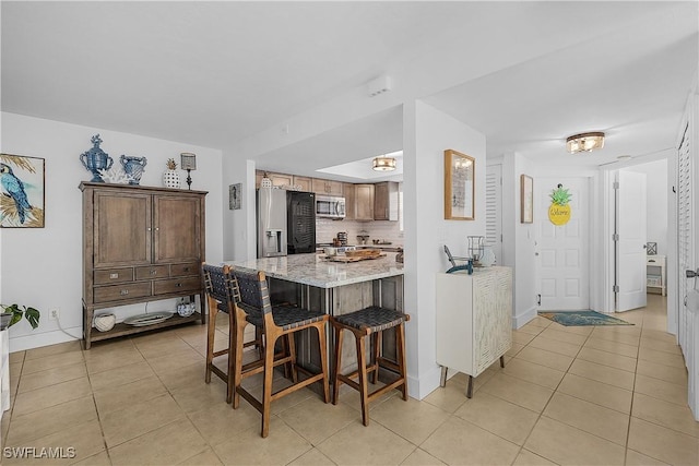 kitchen featuring a breakfast bar area, tasteful backsplash, light stone counters, light tile patterned floors, and appliances with stainless steel finishes