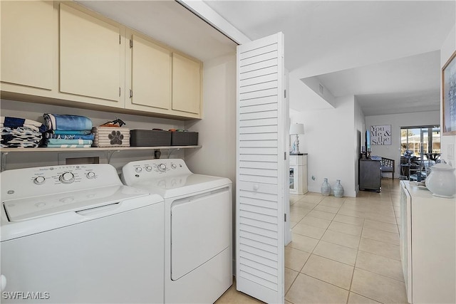 clothes washing area with light tile patterned floors, washing machine and dryer, and cabinets