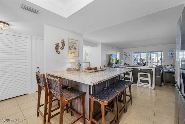 kitchen featuring light stone countertops, a breakfast bar, light tile patterned floors, and kitchen peninsula