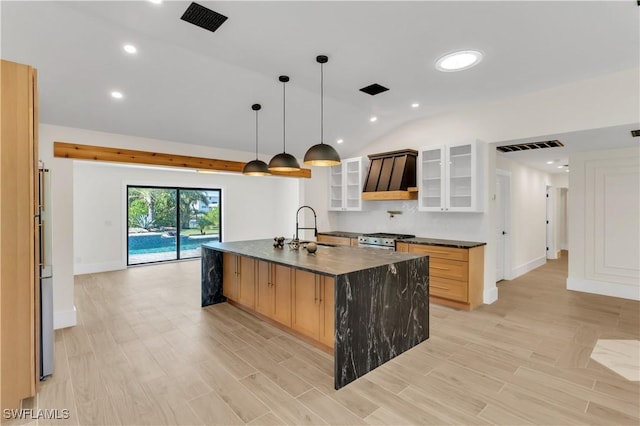 kitchen featuring dark countertops, lofted ceiling, range hood, a kitchen island with sink, and a sink