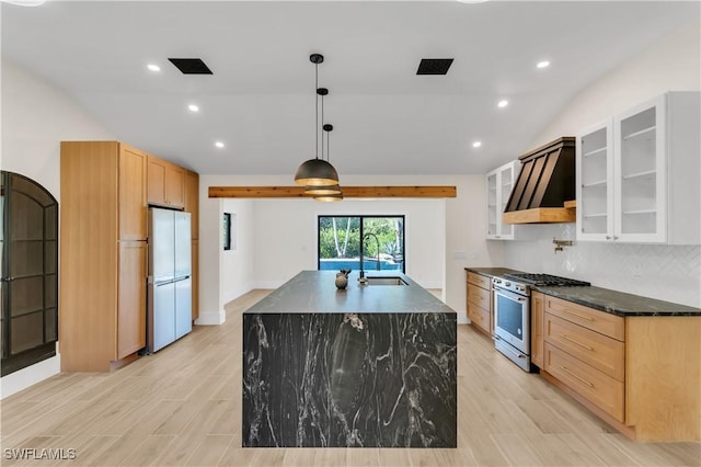 kitchen with a center island with sink, wall chimney exhaust hood, freestanding refrigerator, stainless steel stove, and a sink