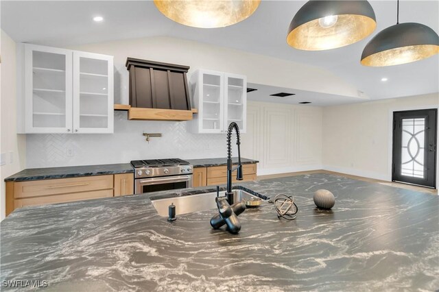 kitchen with lofted ceiling, decorative backsplash, stainless steel range, dark stone countertops, and glass insert cabinets