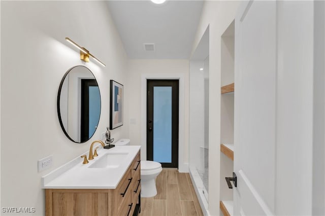 full bath featuring visible vents, toilet, vanity, wood finish floors, and a walk in shower