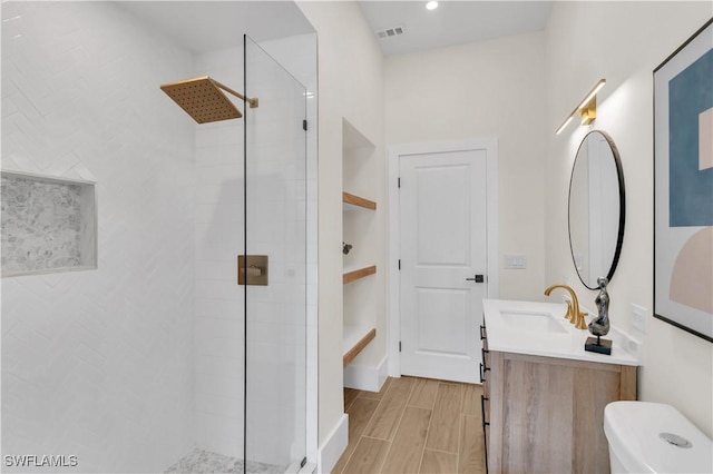 bathroom featuring wood finish floors, visible vents, toilet, a tile shower, and vanity