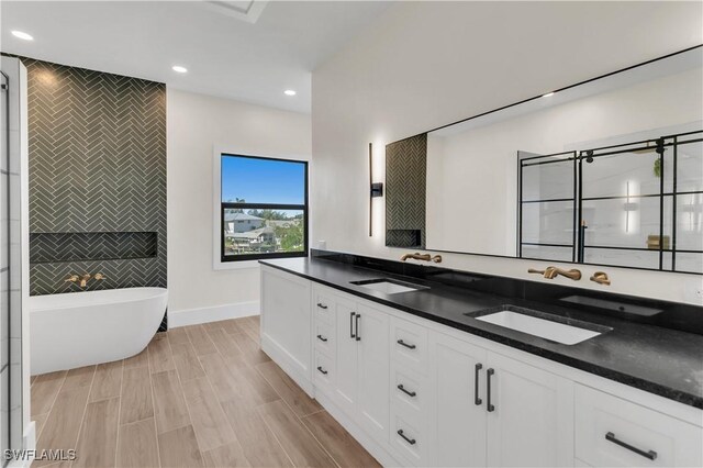 bathroom with a freestanding tub, tile walls, a sink, and recessed lighting