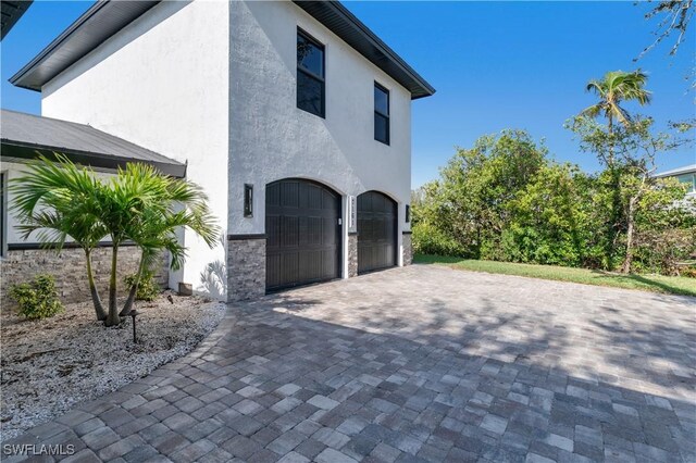 view of side of home featuring an attached garage, stone siding, decorative driveway, and stucco siding