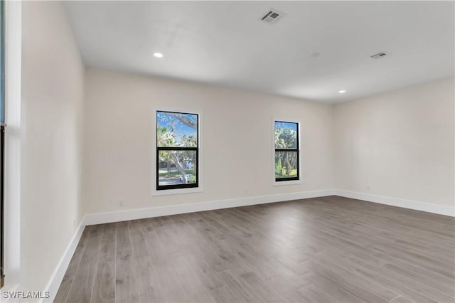 unfurnished room with plenty of natural light, wood finished floors, visible vents, and baseboards