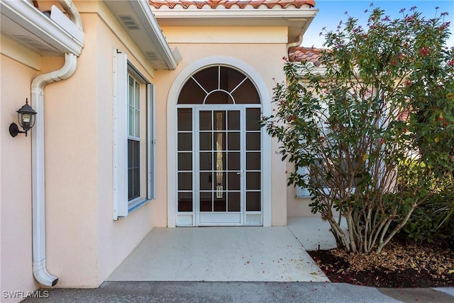 view of exterior entry featuring visible vents, a patio area, a tile roof, and stucco siding